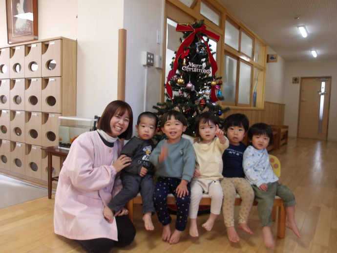 1歳児がクリスマスツリーの前に座っている写真
